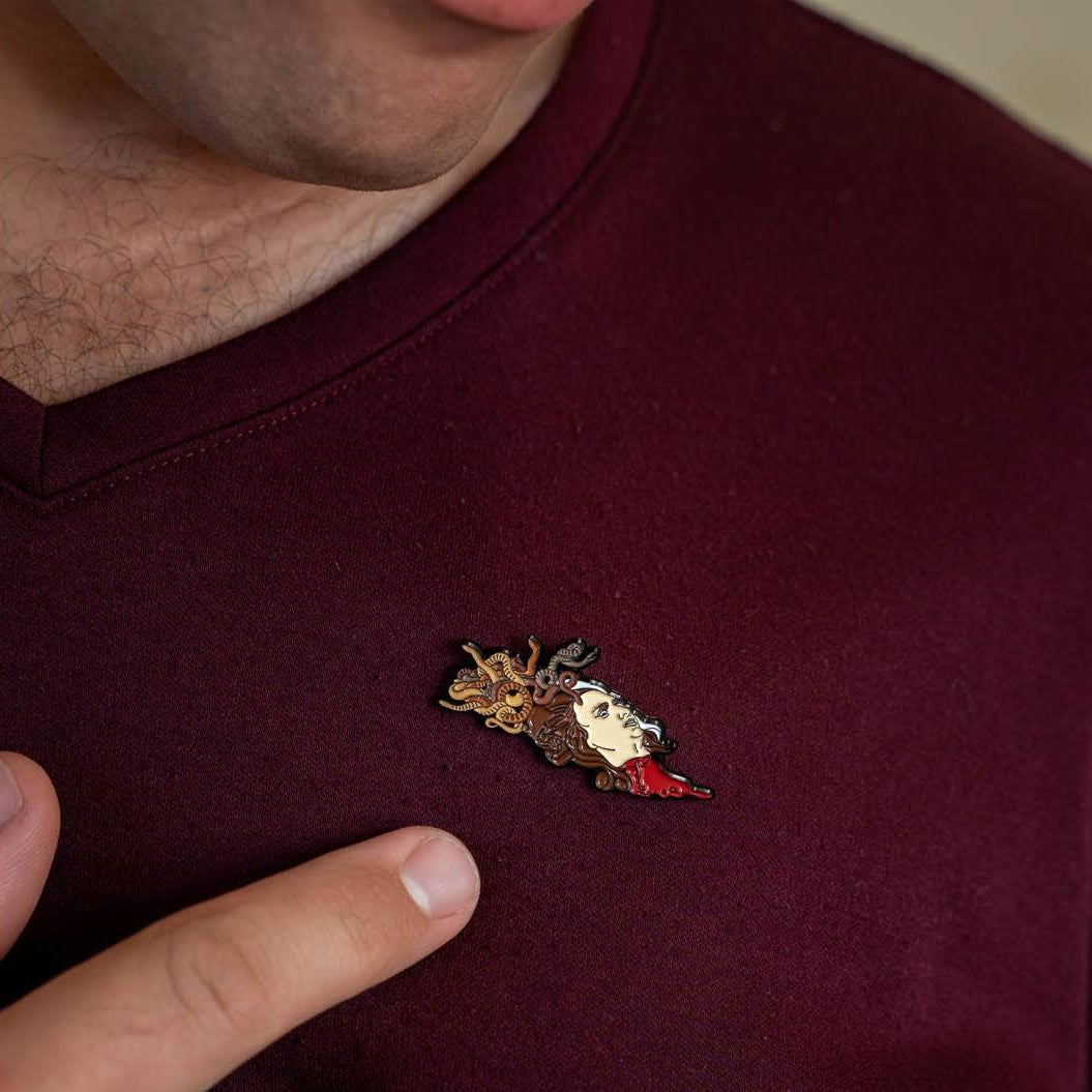 Man in maroon shirt pointing to Medusa enamel pin on his shirt