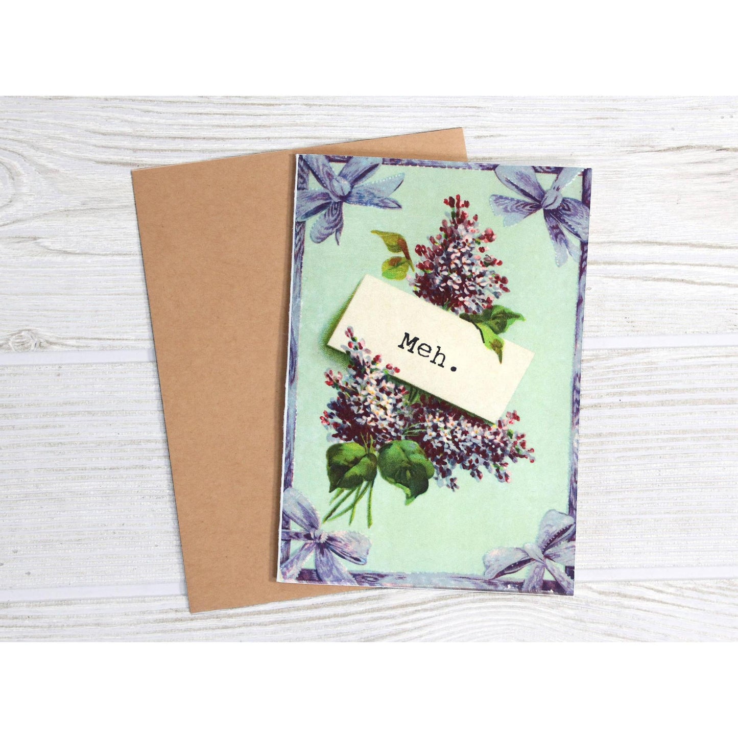 Greeting card with floral design and 'Meh' text on a wooden surface