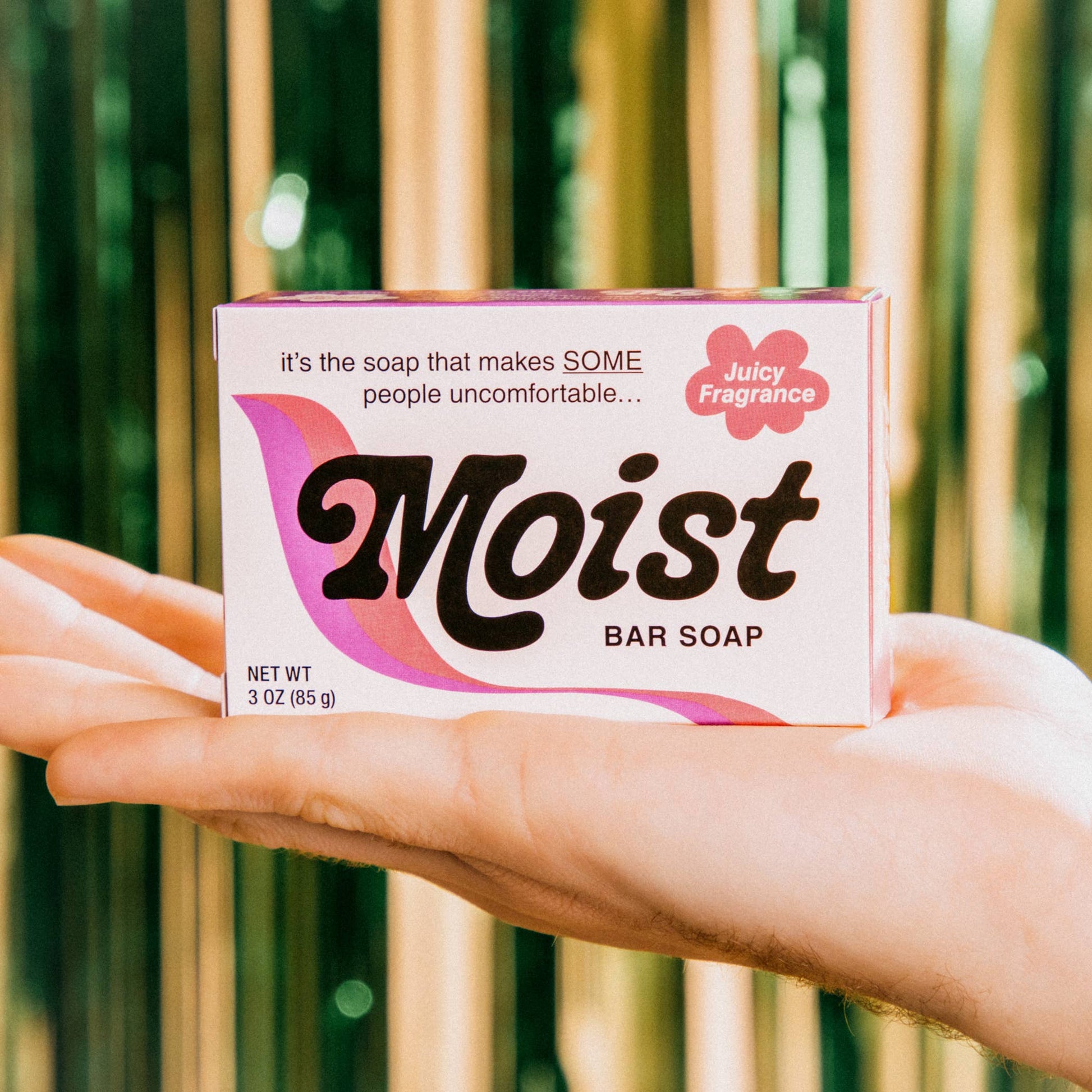 Hand holding a box of 'Moist' bar soap with a bamboo background