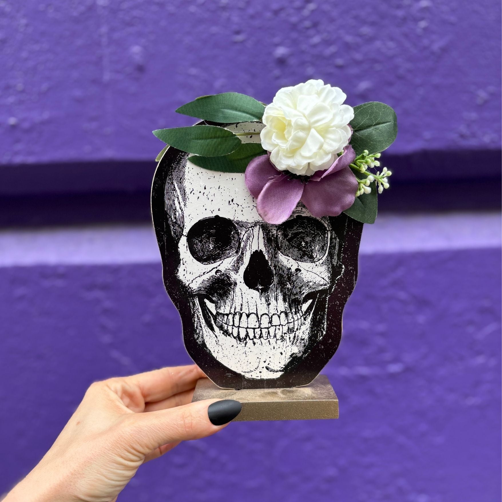 Skull decoration with flowers held against a purple background