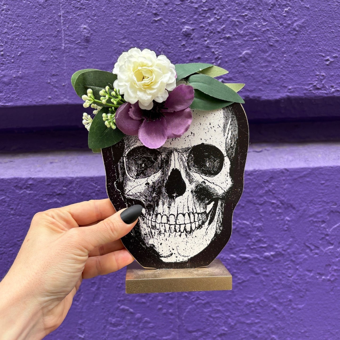Skull-shaped wood decor with flowers against a purple background