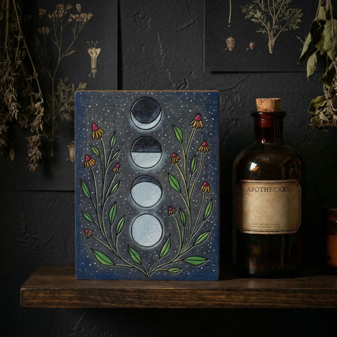 Decorative moon phase panel with flowers on a shelf against a dark wall with botanical illustrations.