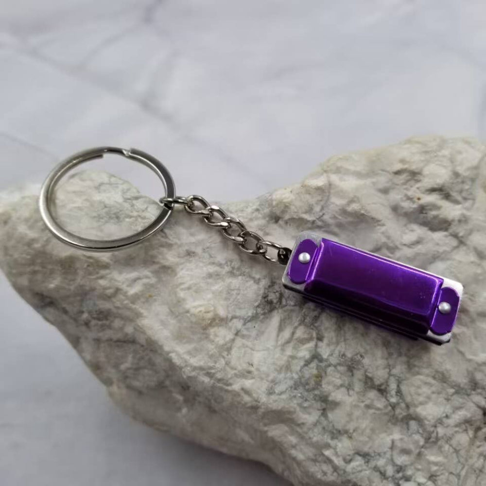 Purple harmonica keychain with a small tool on a stone surface