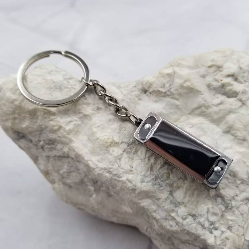 Silver metallic harmonica keychain on a textured stone surface