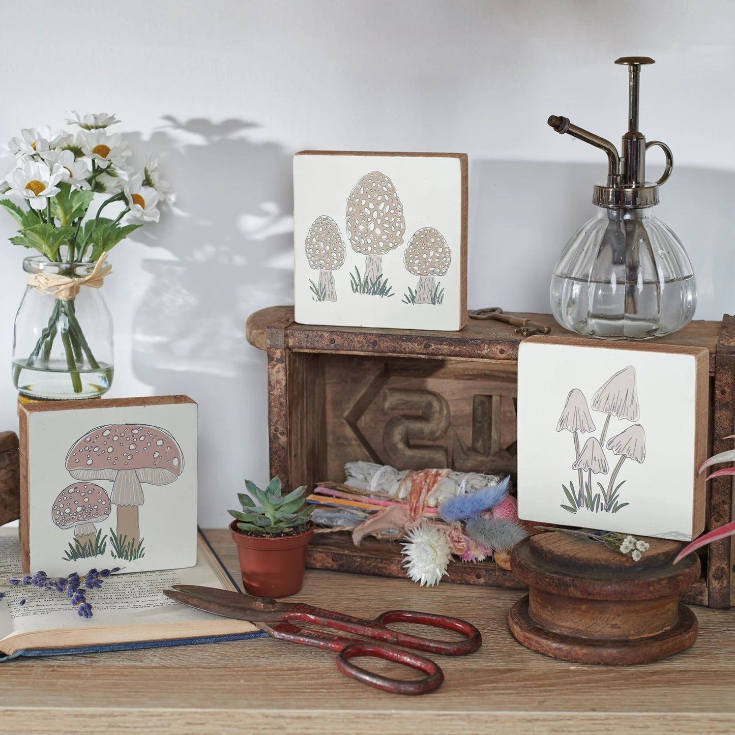 Decorative setup with framed artwork of mushrooms, a vase with flowers, and a wooden box.