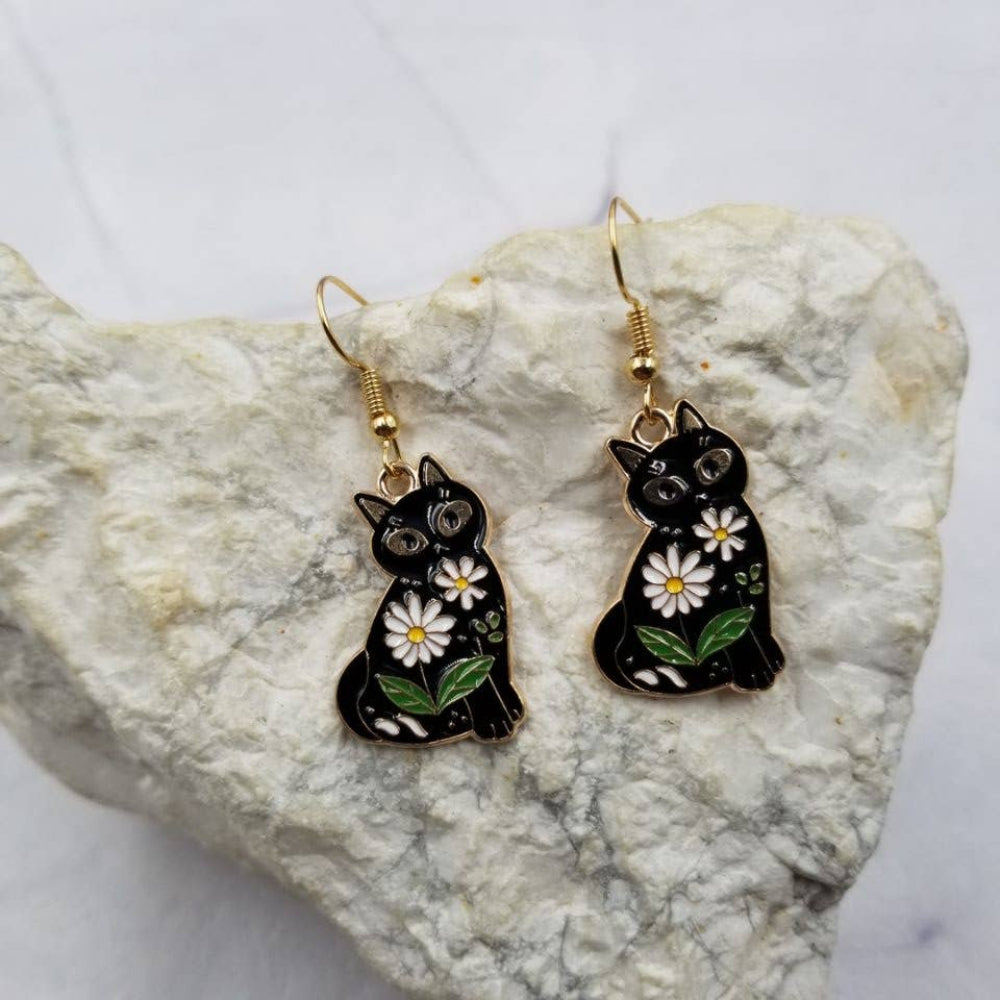 Black cat earrings with floral details on a stone surface