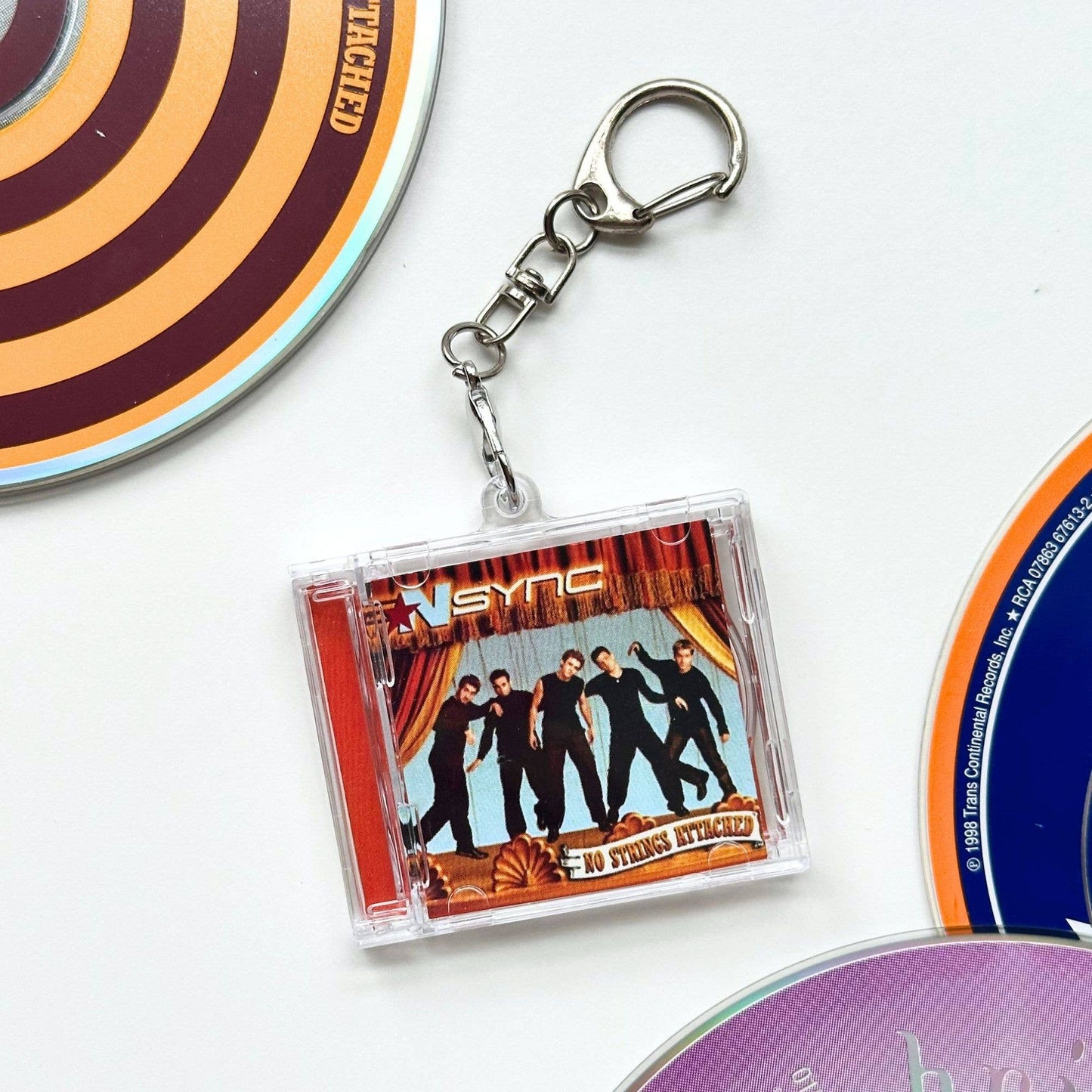 A clear acrylic keychain featuring a Nsync 'No Strings Attached' CD cover print, attached to a silver metal split ring and clasp