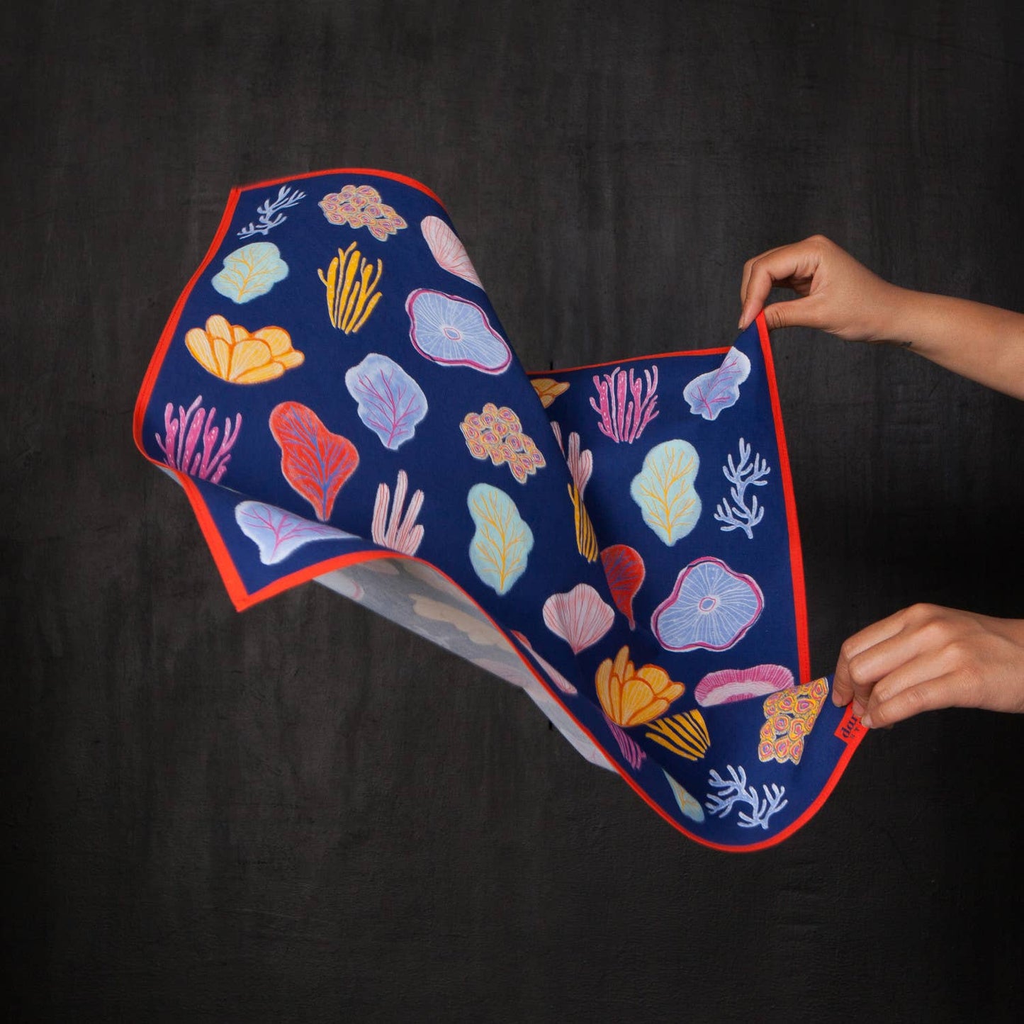 Bandana with coral reef design held by a person against a black background
