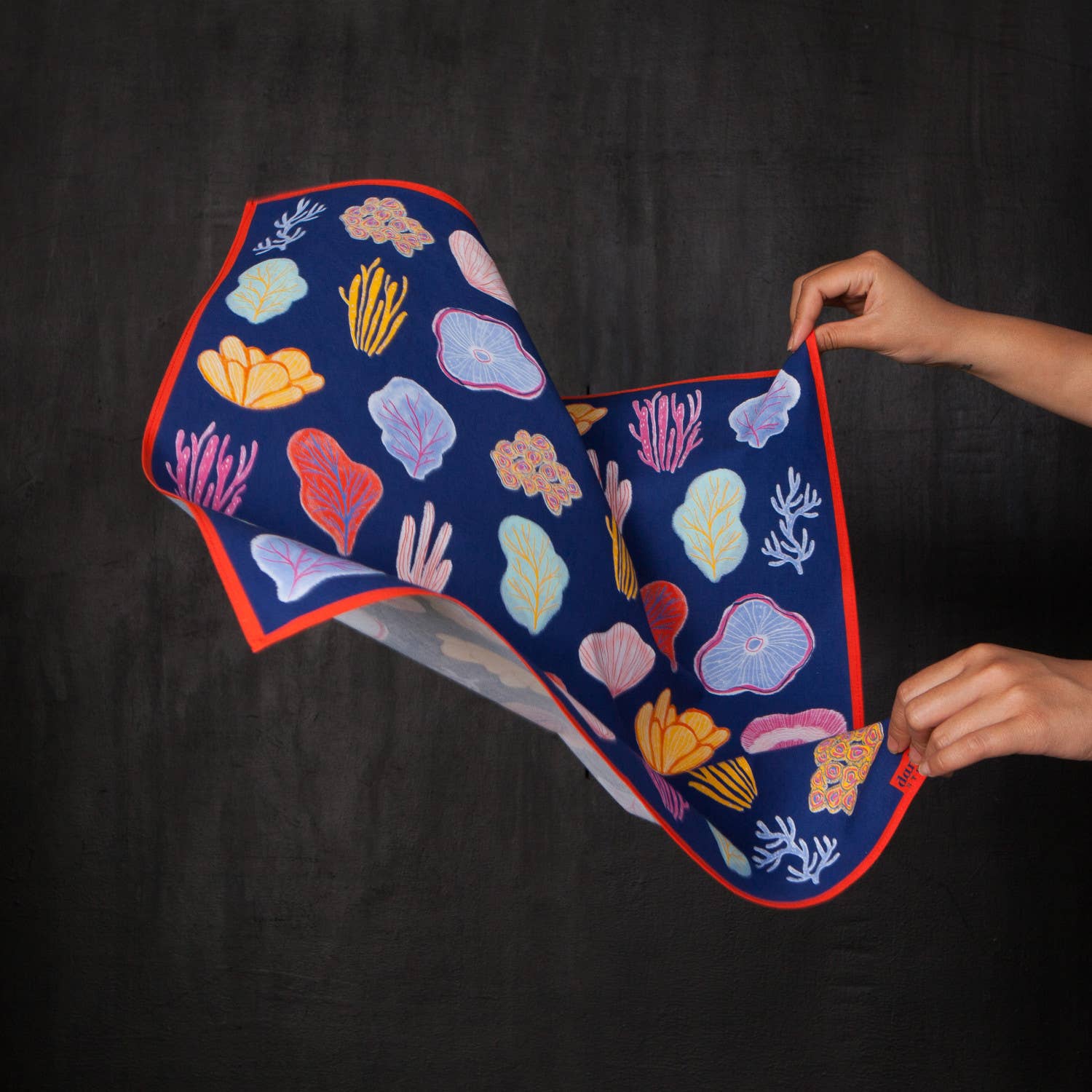 Bandana with coral reef design held by a person against a black background