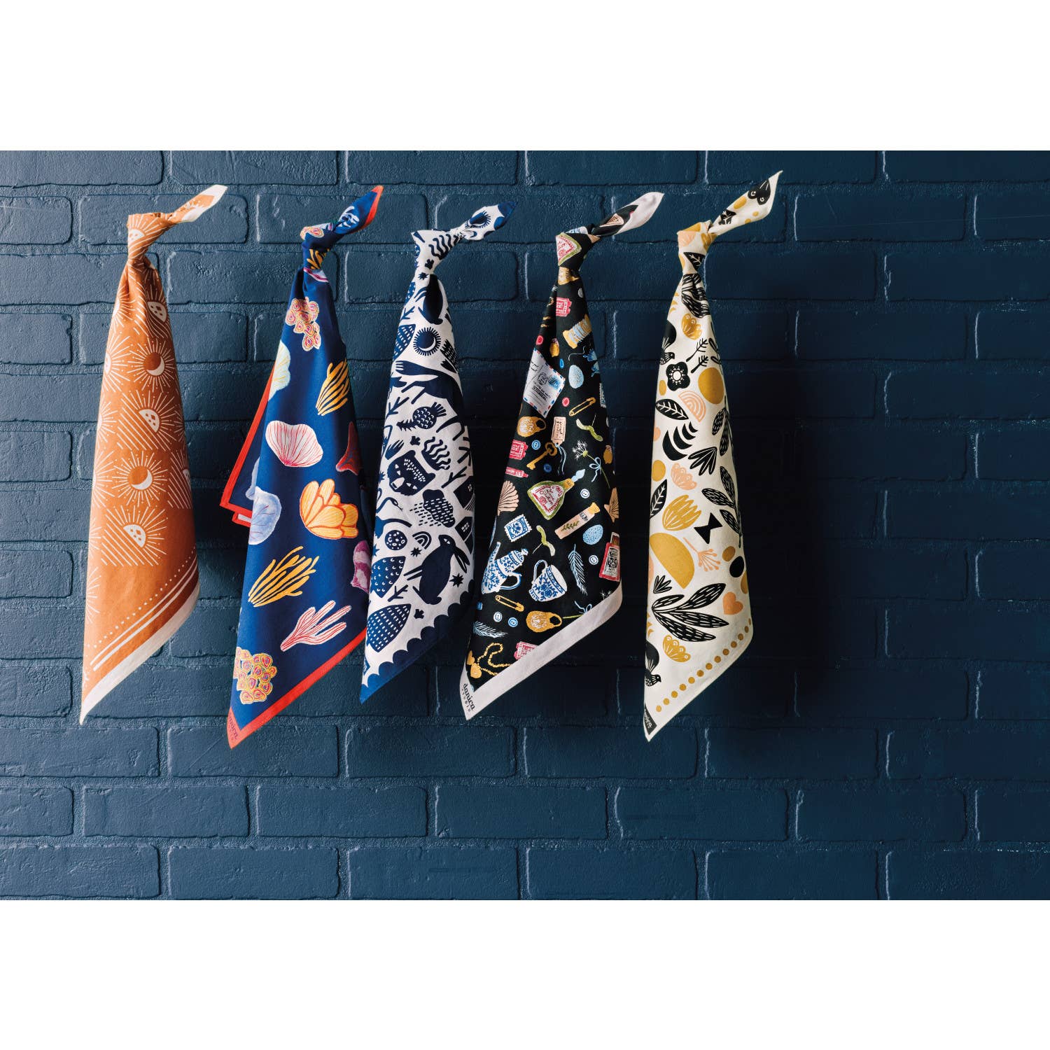 Five colorful bandanas hanging against a dark blue brick wall.
