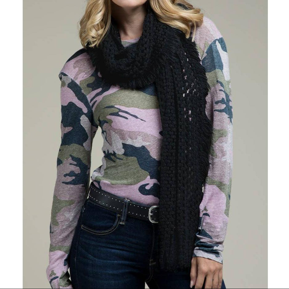 Woman wearing a camouflage sweater and black scarf against a neutral background