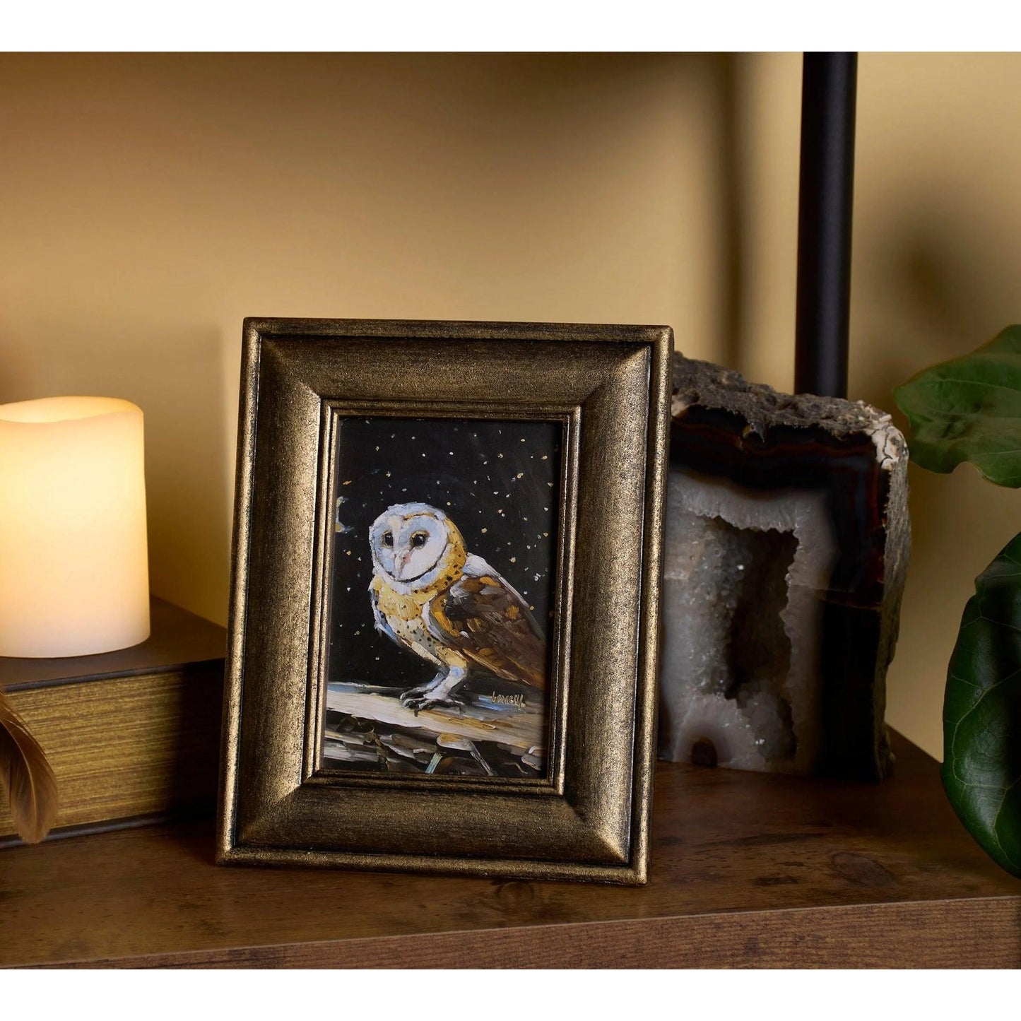 Framed artwork of an owl on a shelf with a candle and decorative rock.