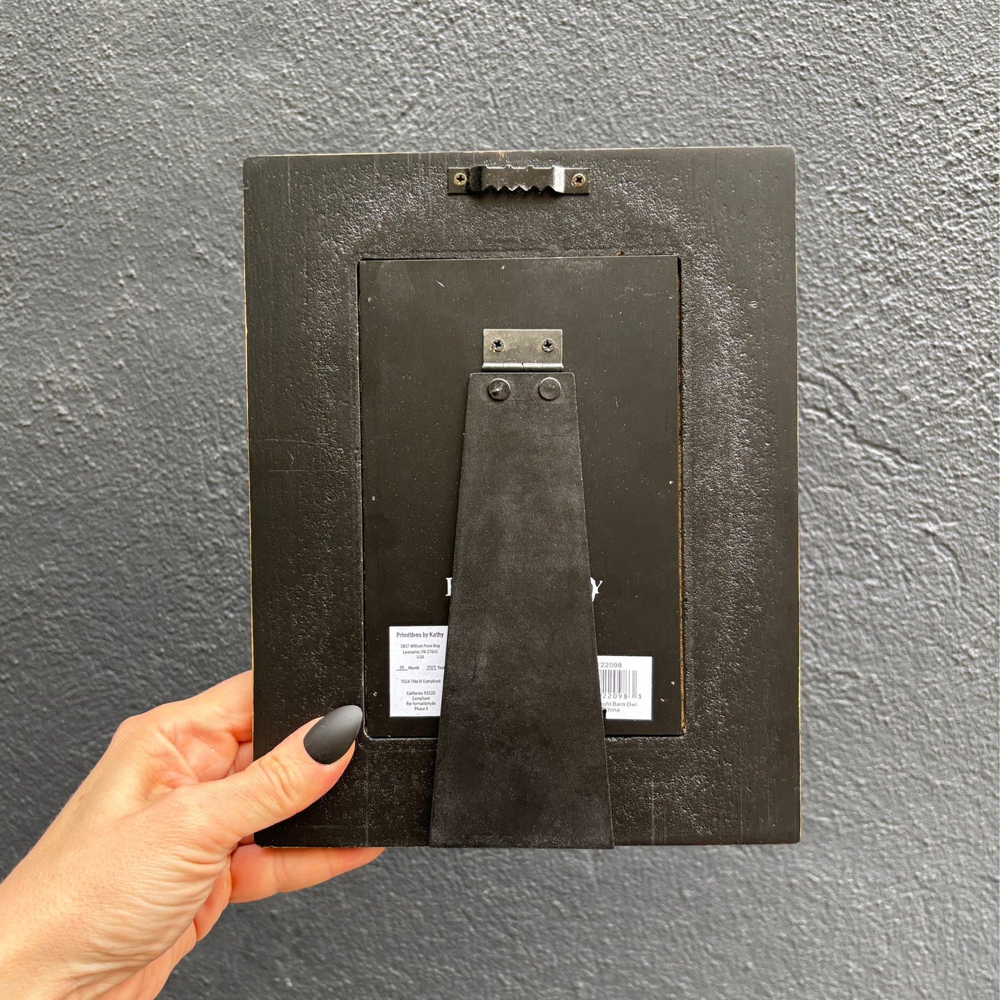 Person holding a black picture frame against a gray wall