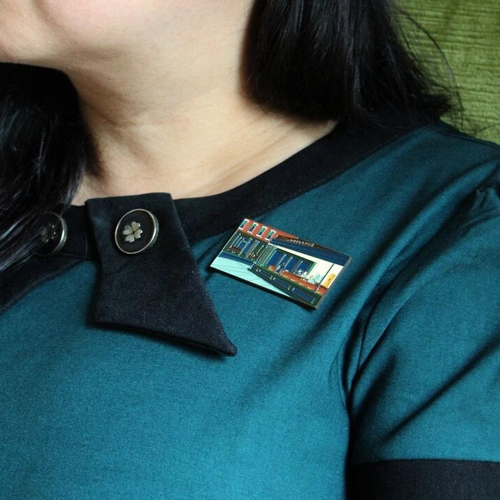 Close-up of a person wearing a teal shirt with a black collar and a badge on a green background