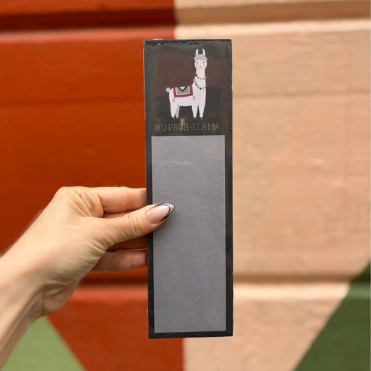 Hand holding a notepad with a llama illustration against a wooden background