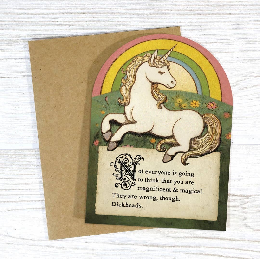 Greeting card with unicorn illustration and humorous text on a wooden surface