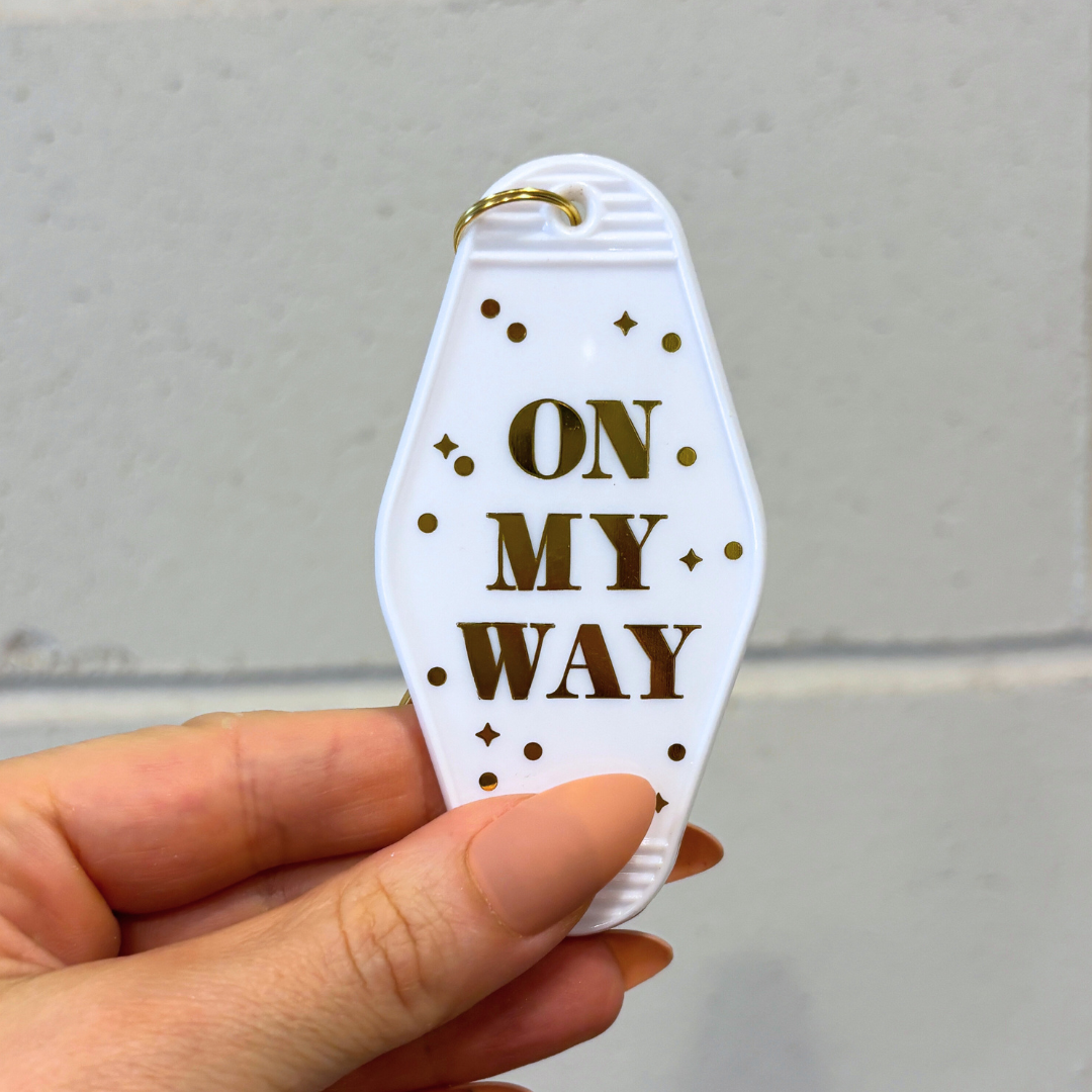 Keychain with 'On My Way' text held by a hand against a neutral background