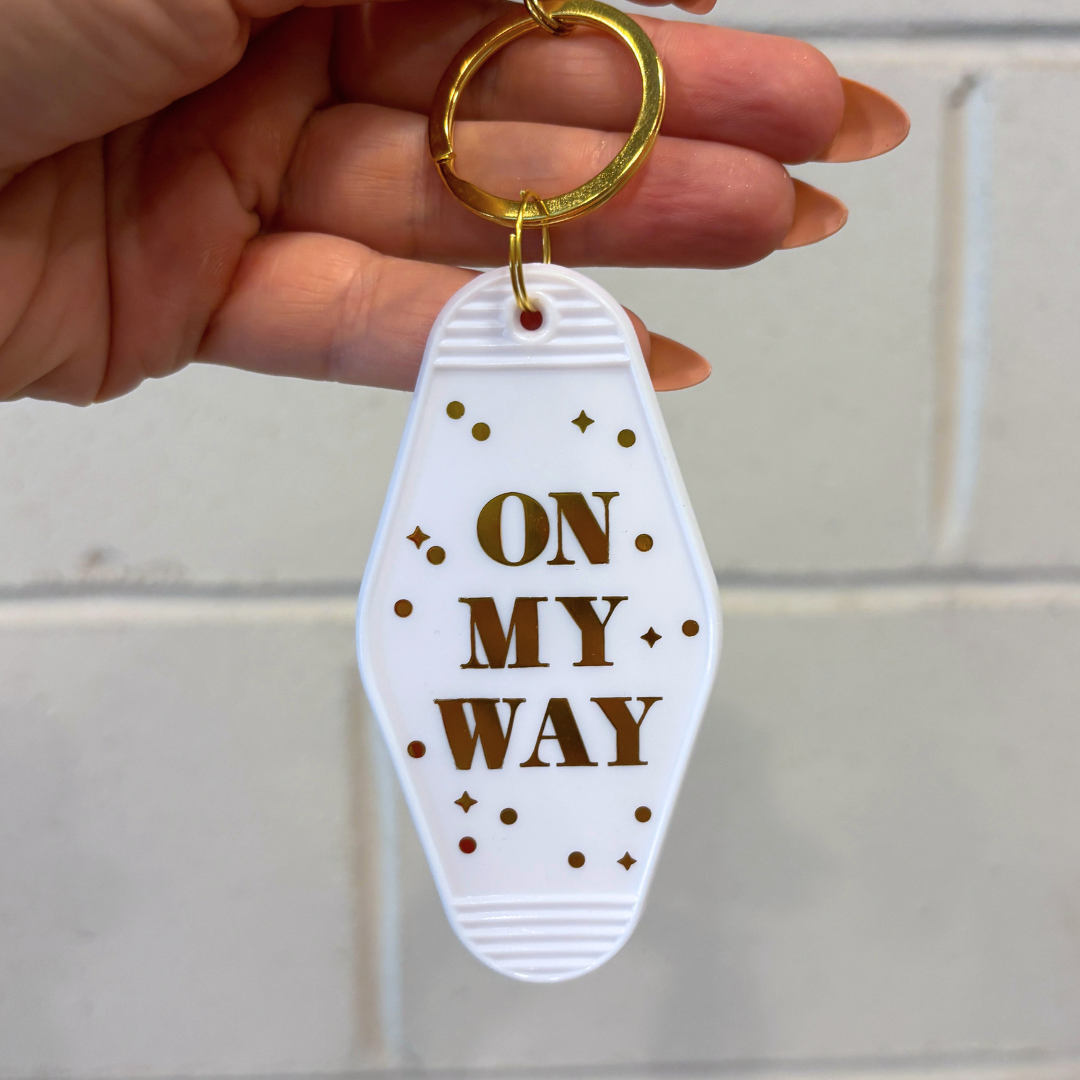 Keychain with 'On My Way' text held by a hand against a tiled wall background
