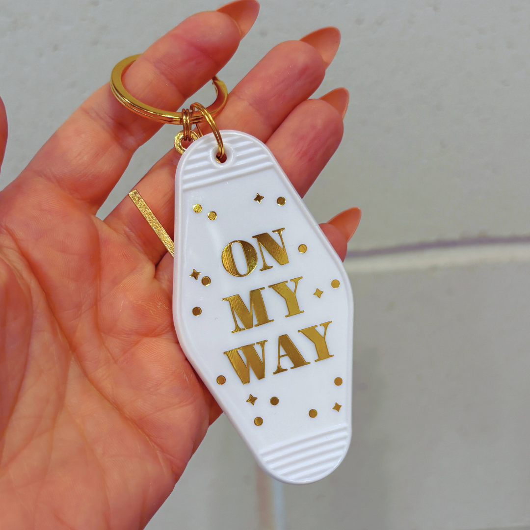 Keychain with 'On My Way' text held by a hand against a neutral background