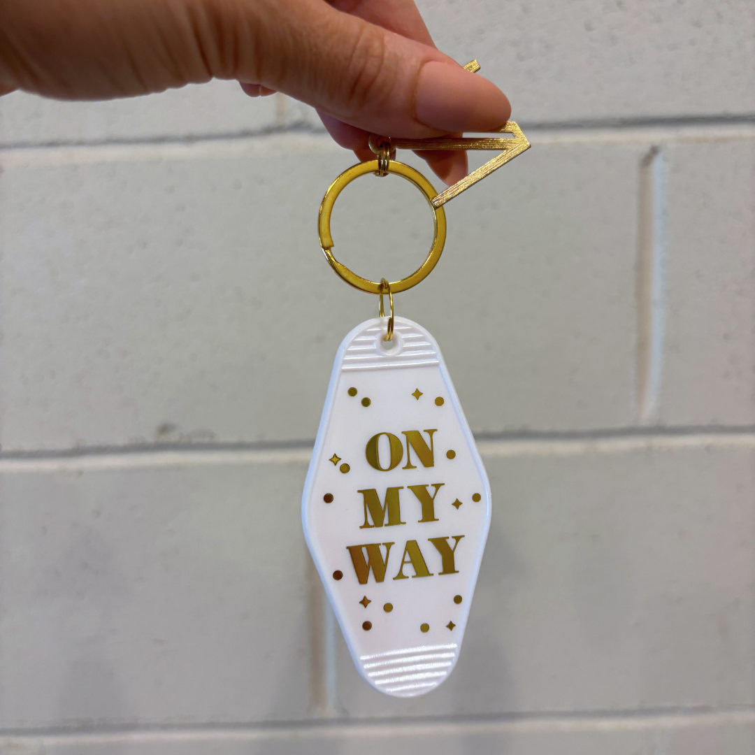 Keychain with 'On My Way' text held by a hand against a light gray background