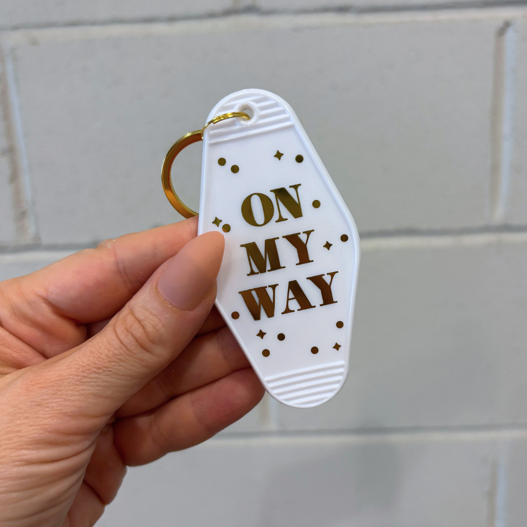 Keychain with 'On My Way' text held by a hand against a tiled wall background