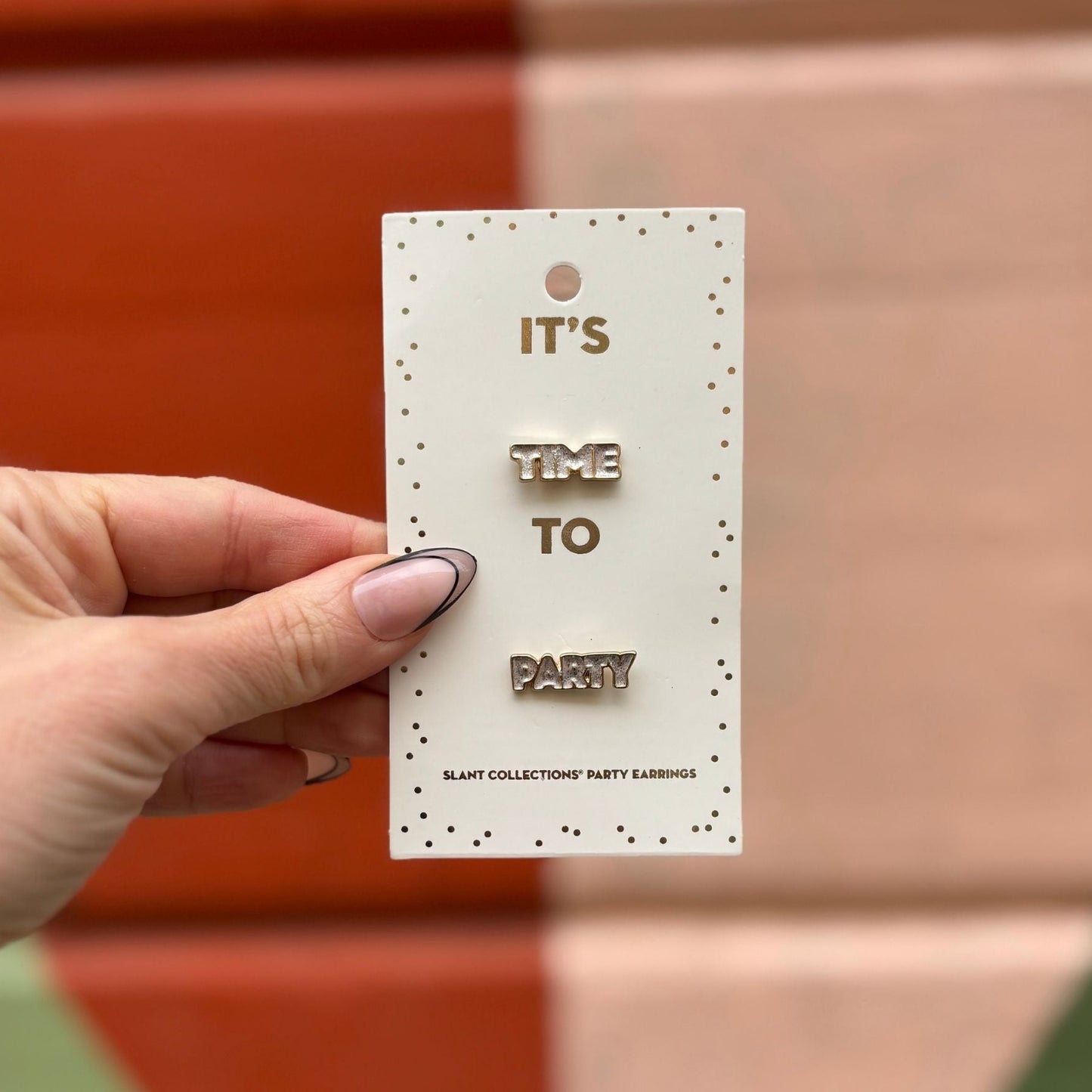Hand holding a card with earrings and 'It's Time to Party' text against a blurred background