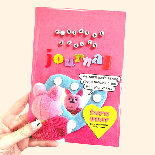 Pink 'Personal Growth Journal' held by a hand with a cartoon character on the cover.