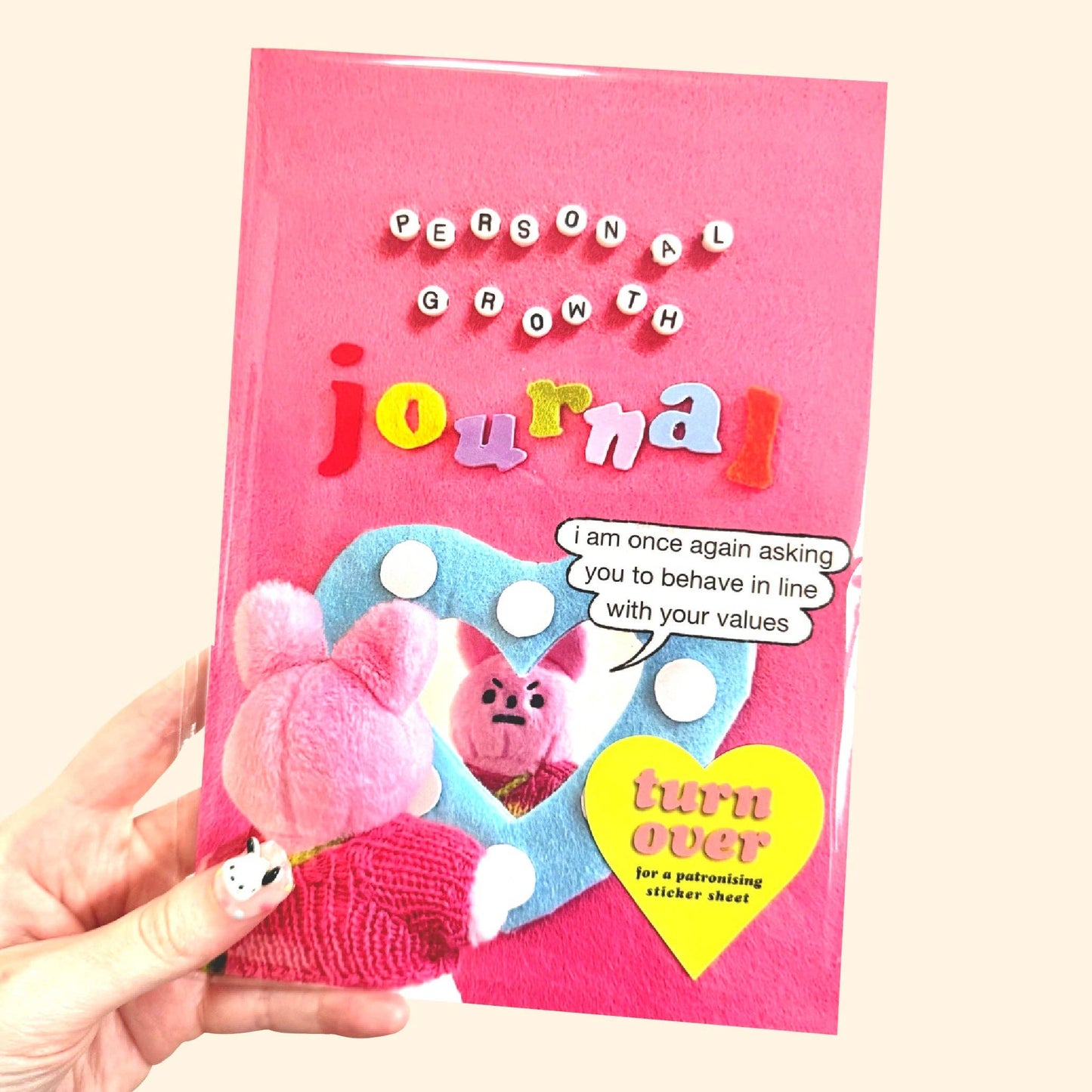 Pink 'Personal Growth Journal' held by a hand with a cartoon character on the cover.