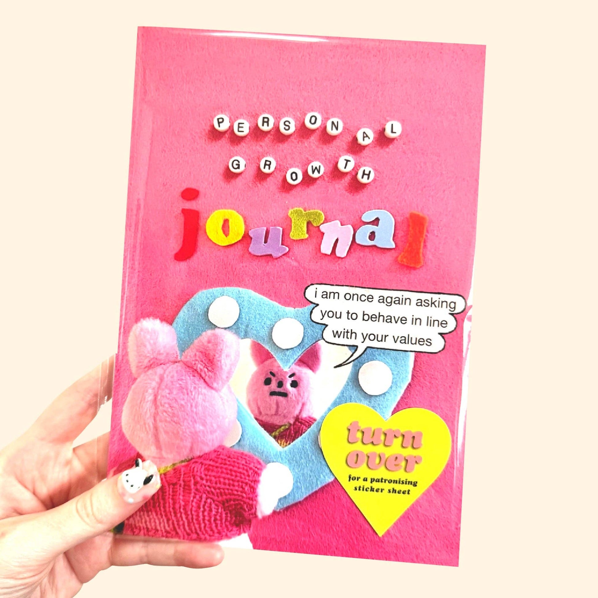 Pink 'Personal Growth Journal' held by a hand with a cartoon character on the cover.