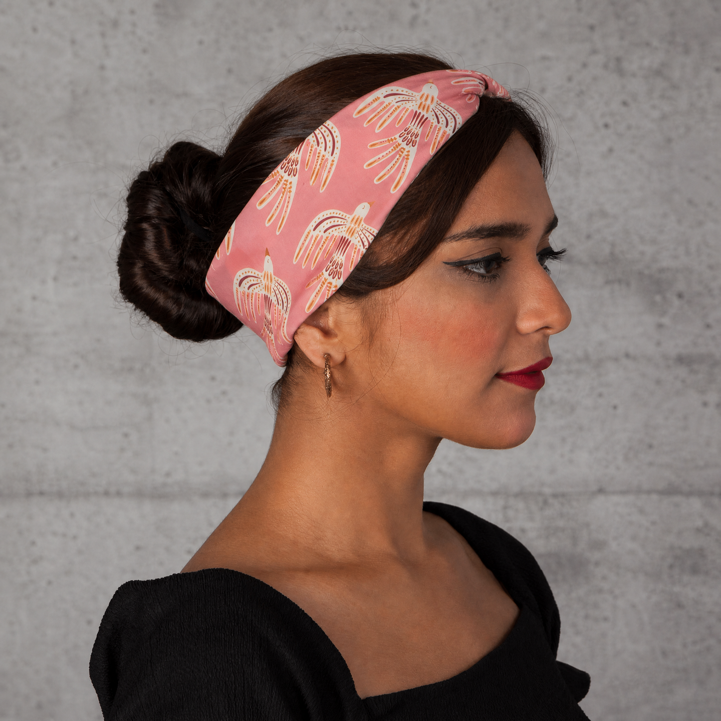 Woman wearing a pink recycled cotton bandana with white bird designs as a headband.