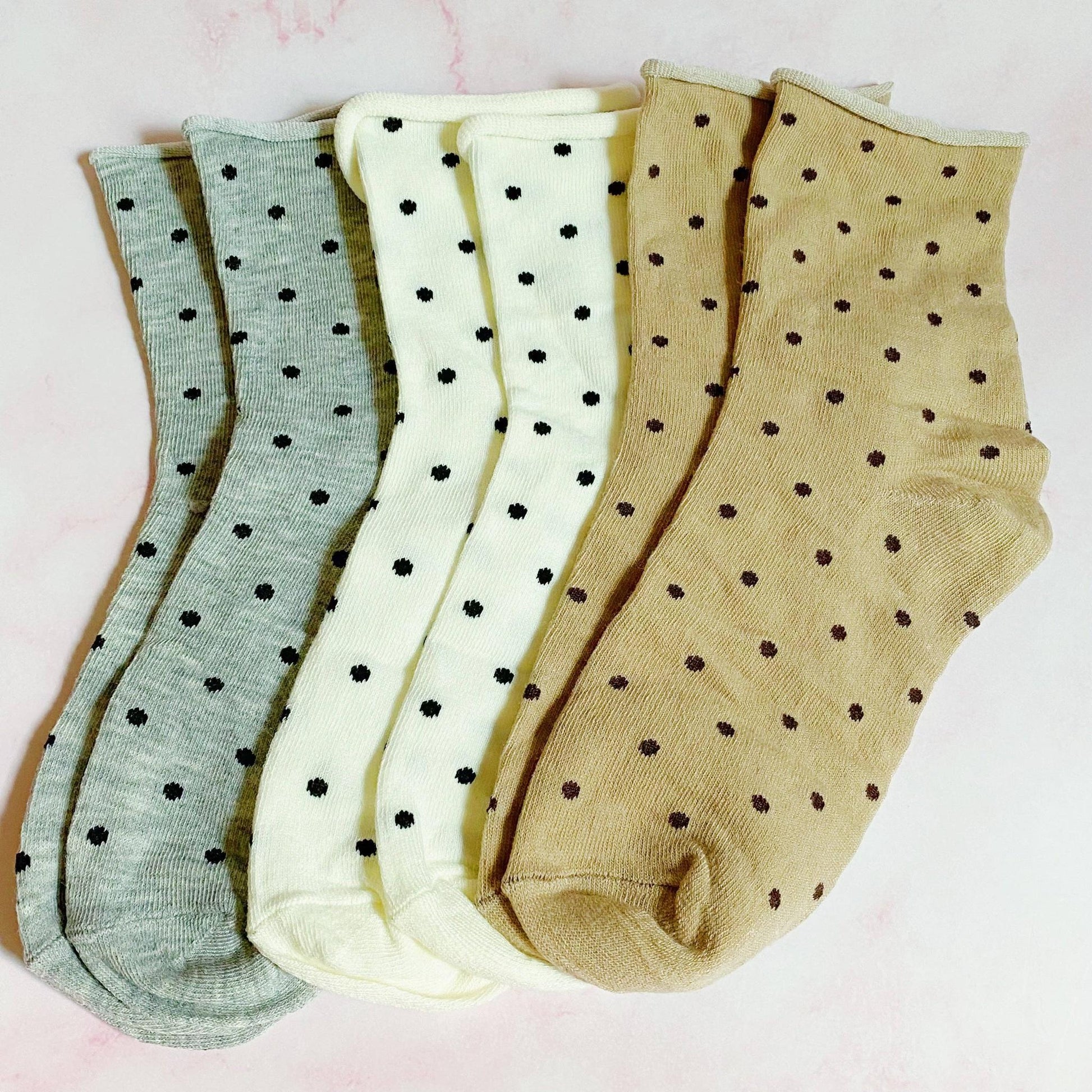 Three pairs of polka dot socks in green, white, and beige on a light pink background