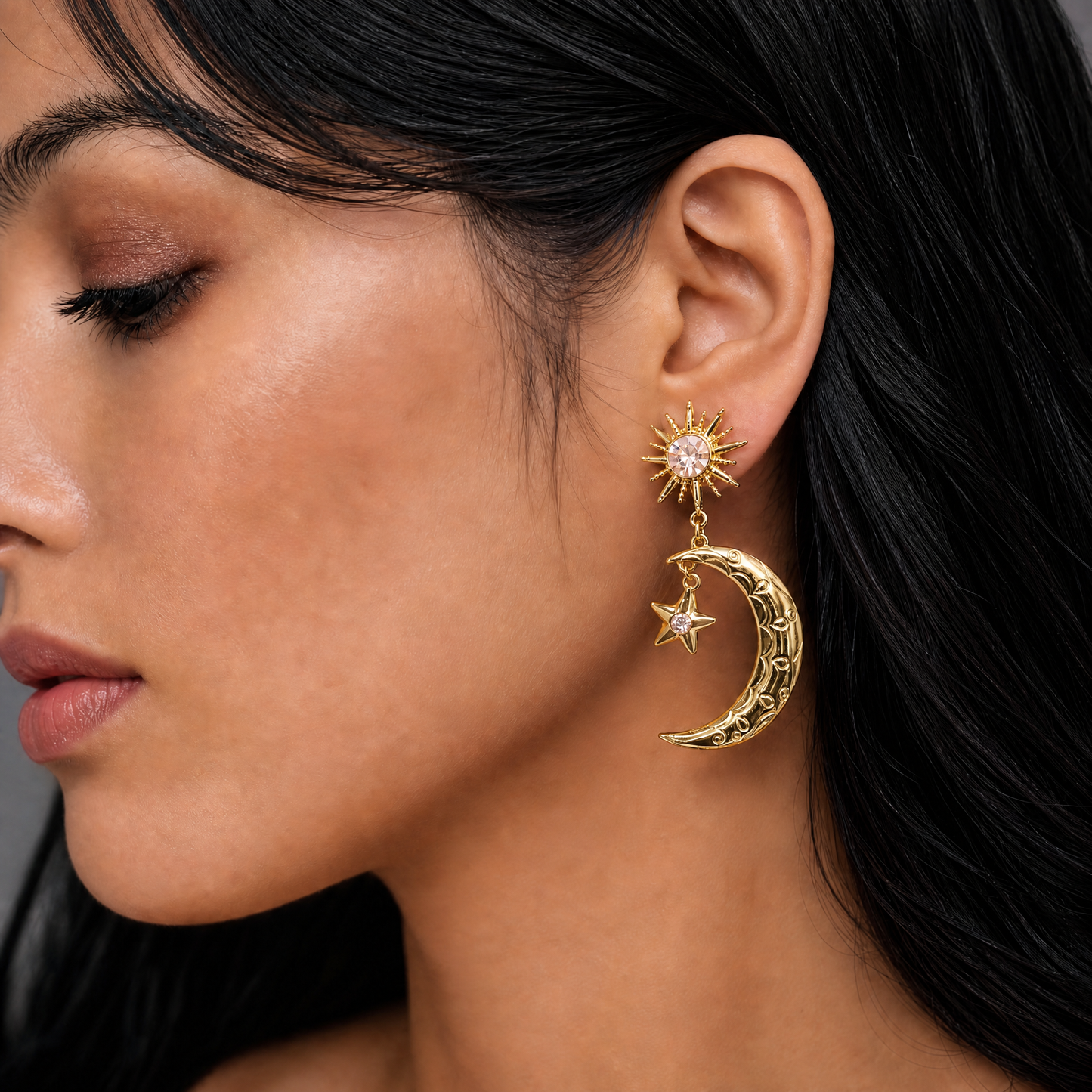 Close-up of a woman wearing gold earrings with a star, moon, and sun design.