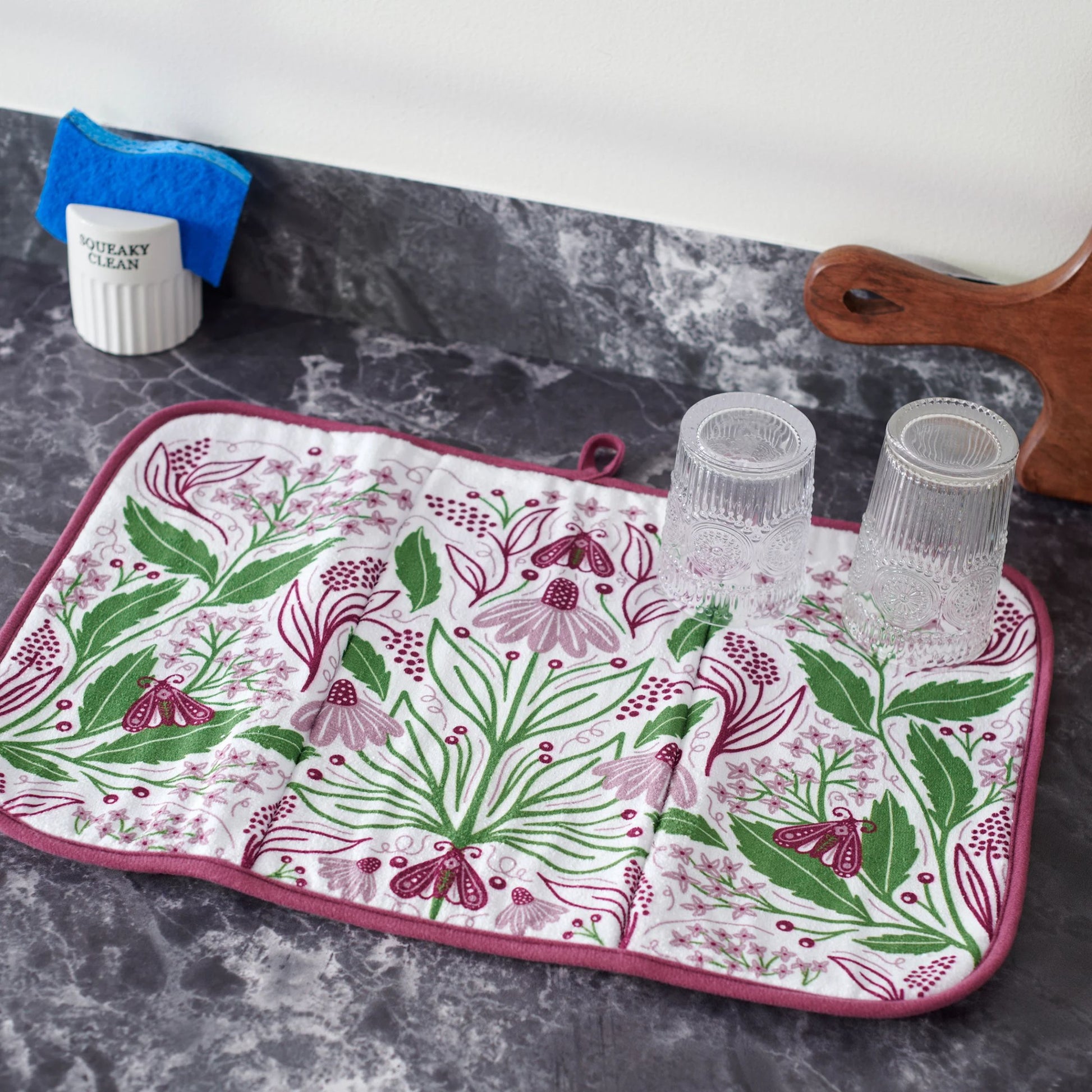 Floral-patterned drying mat on a kitchen counter with glasses and a towel.