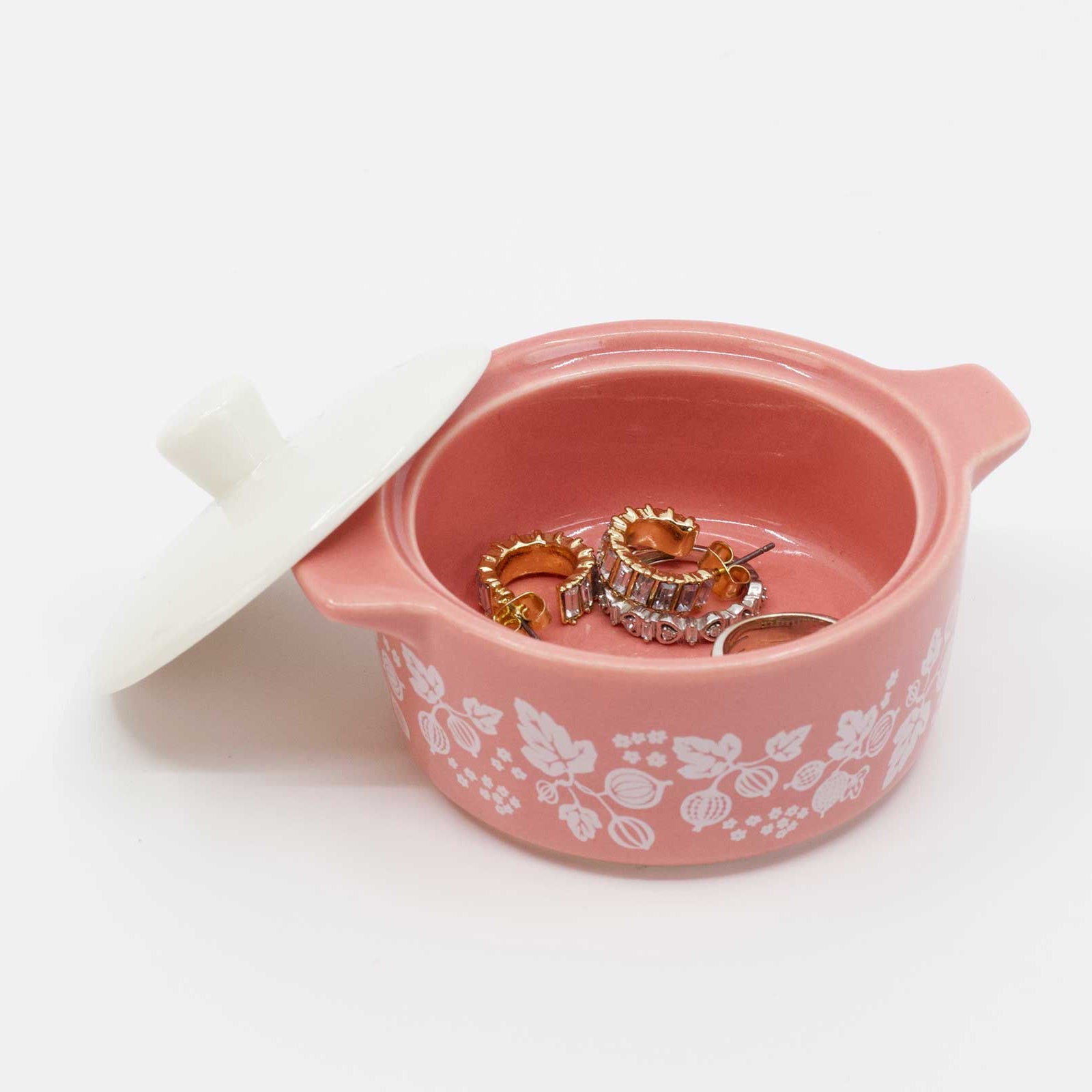 Pink jewelry box with floral patterns containing two rings on a white background