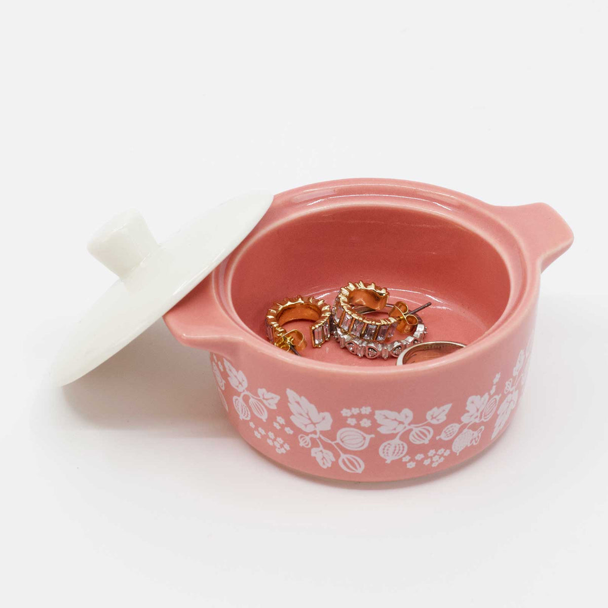 Pink jewelry box with floral patterns containing two rings on a white background