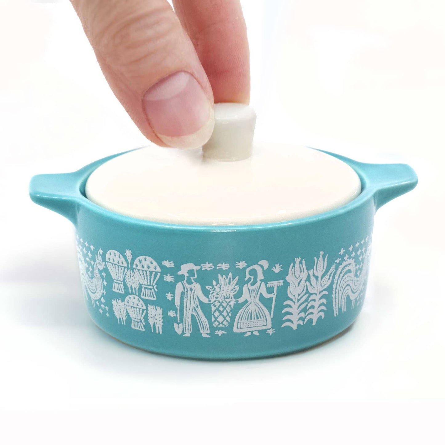 Small Pyrex-inspired blue container with white lid being held by a hand on a white background