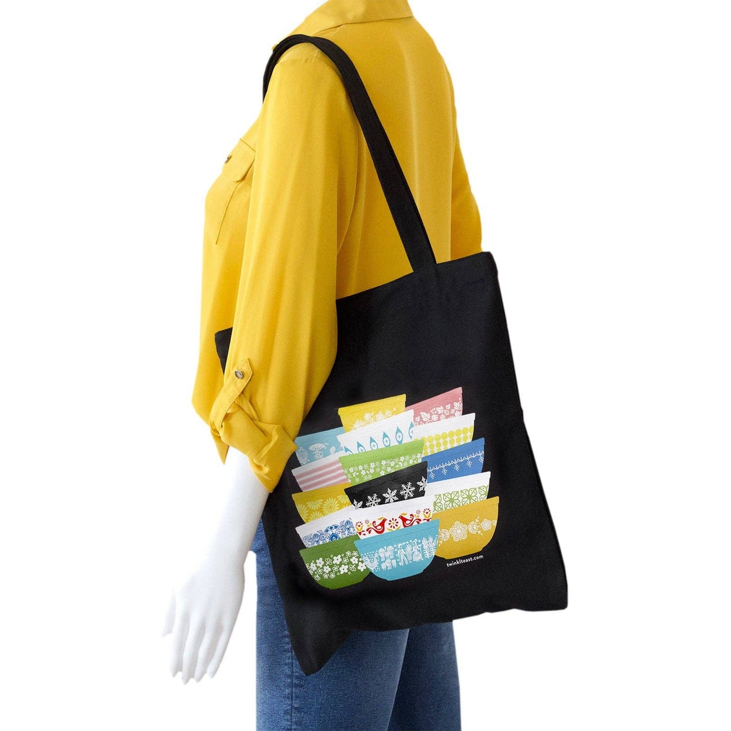 Black tote bag with colorful bowls design held by a person wearing a yellow shirt and blue jeans on a white background