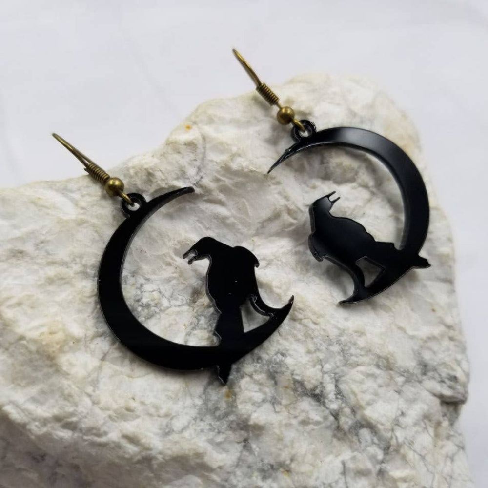 Black crescent moon and raven earrings on a textured white surface
