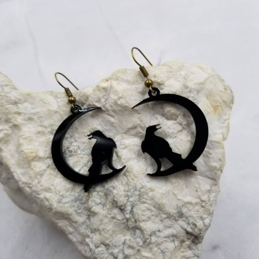 Black raven earrings on a white stone surface