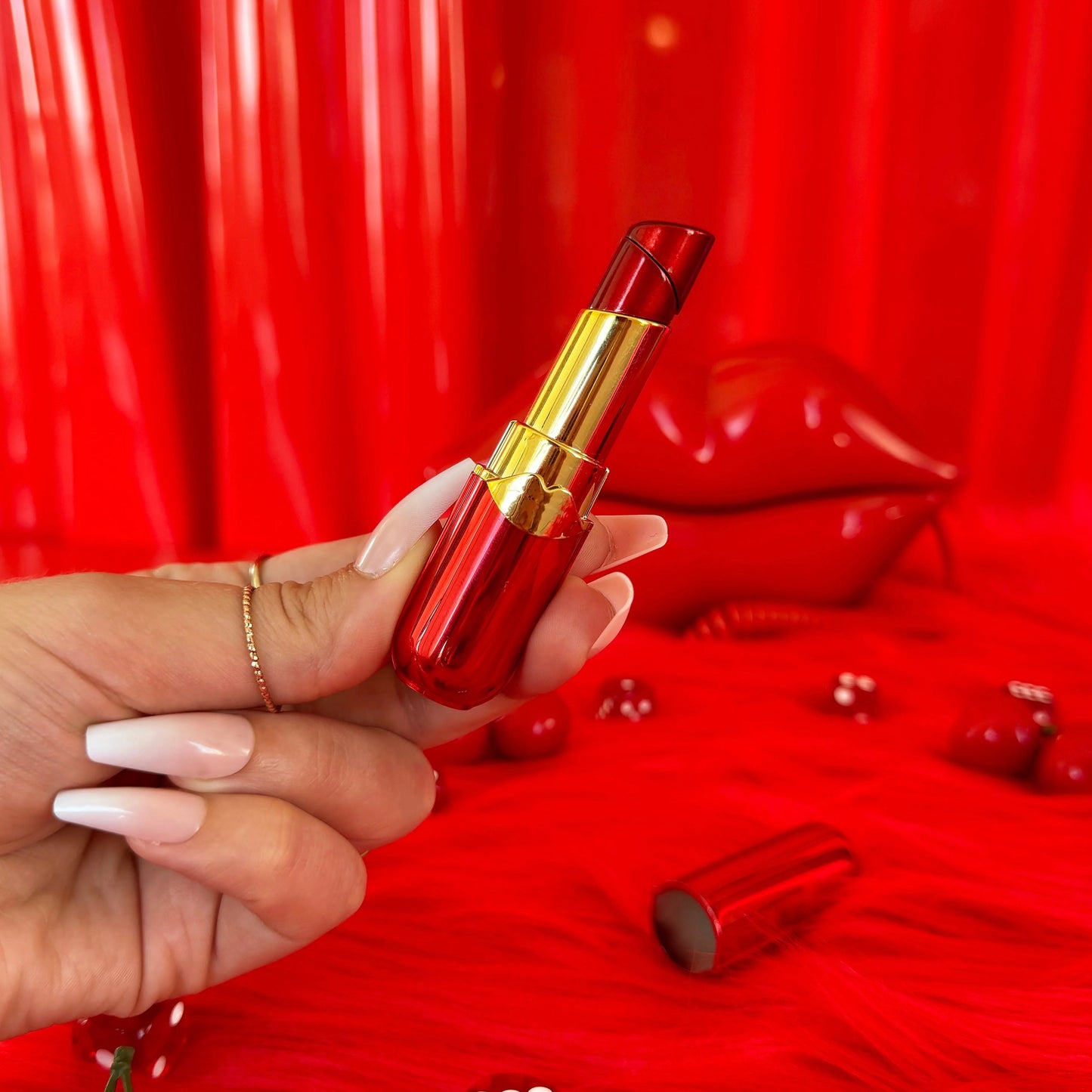 Red lipstick shaped lighter held by a hand with a red background