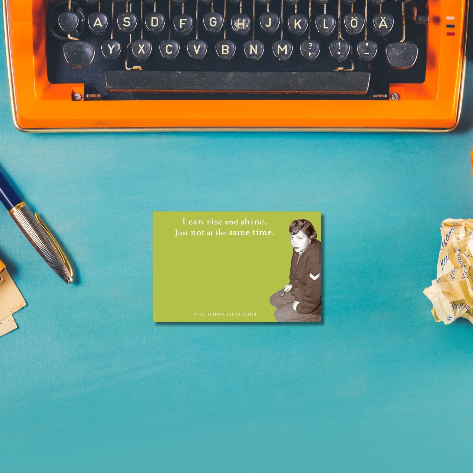 Vintage typewriter on a blue surface with a motivational sticky note featuring a retro lady and text.