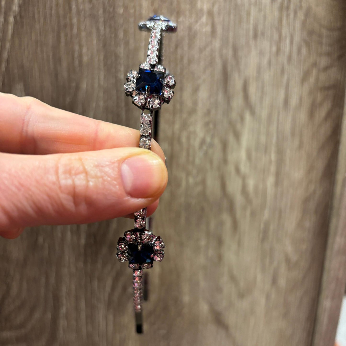 A jeweled headband held by a hand against a wooden surface