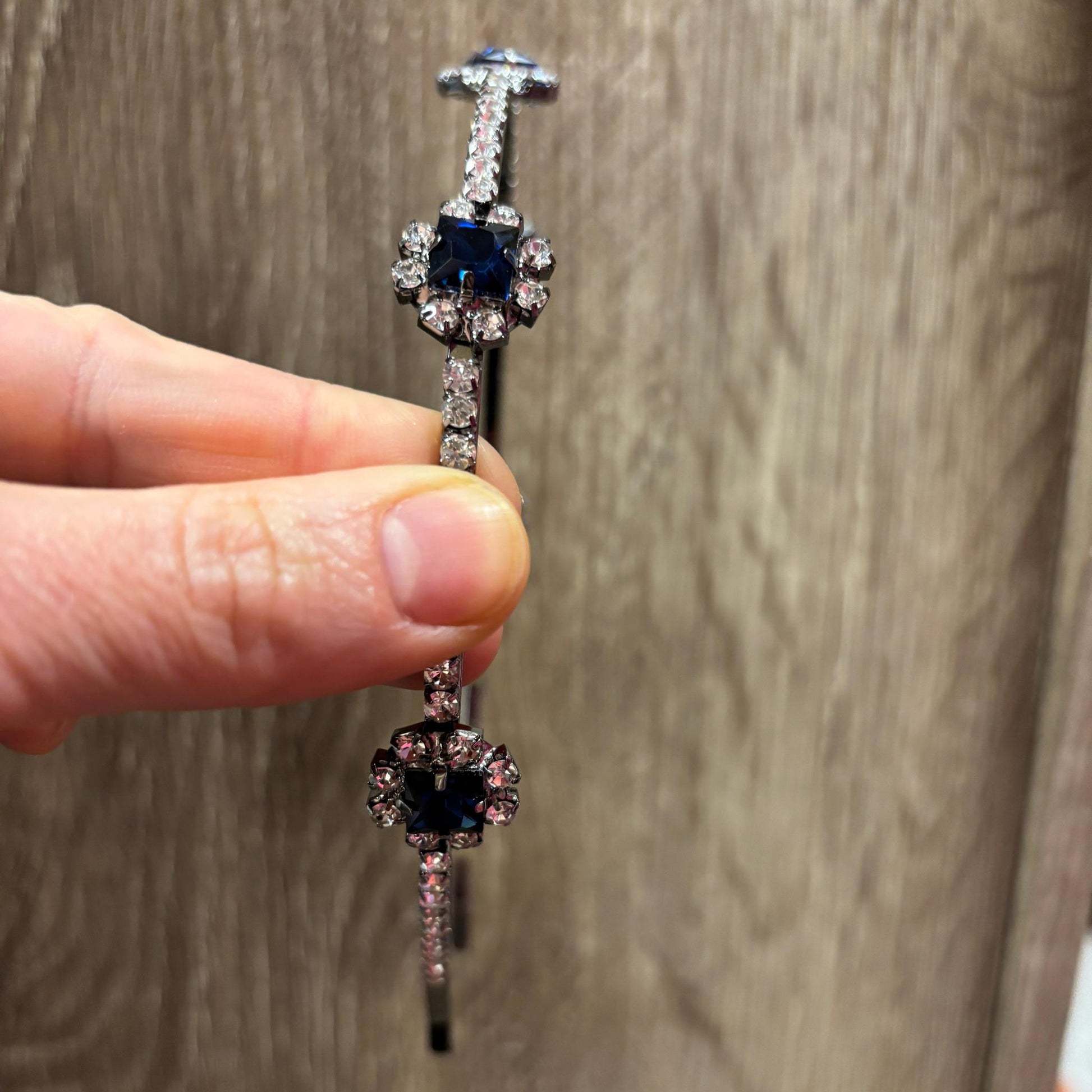 A jeweled headband held by a hand against a wooden surface