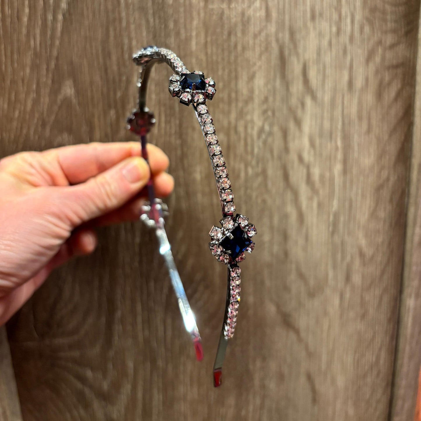 Decorative headband with gemstones held by a hand on a wooden surface