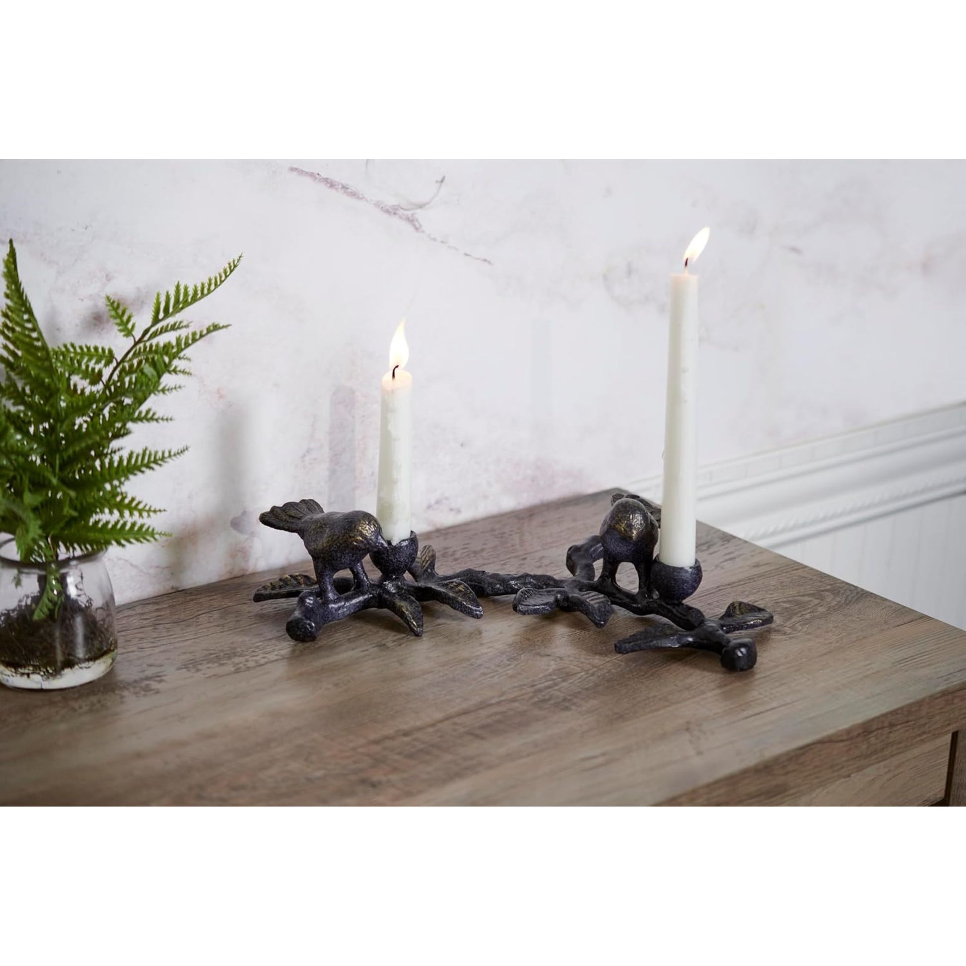 Decorative candle holders with candles on a wooden surface next to a plant.