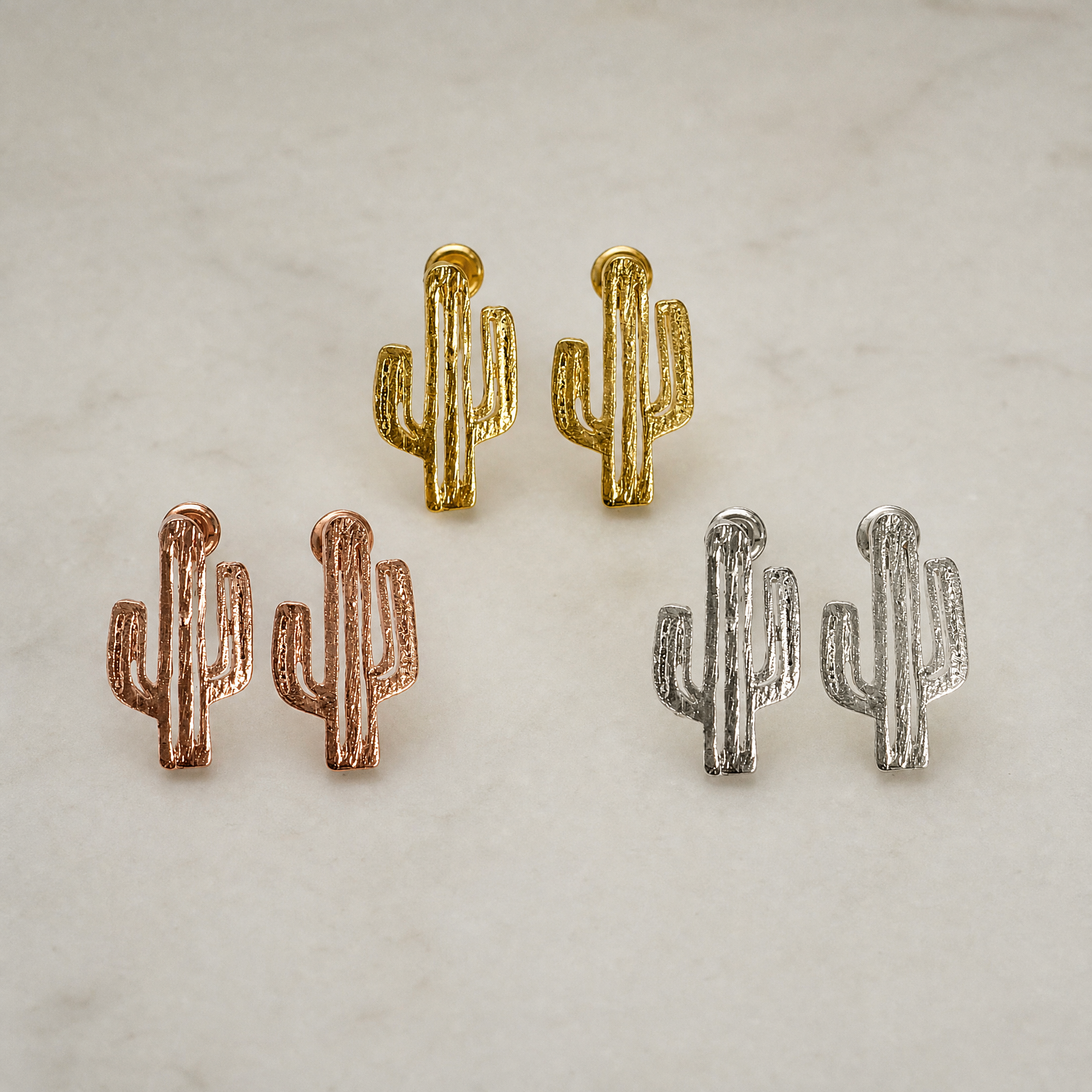 Cactus-shaped earrings in gold, rose gold, and silver on a light background