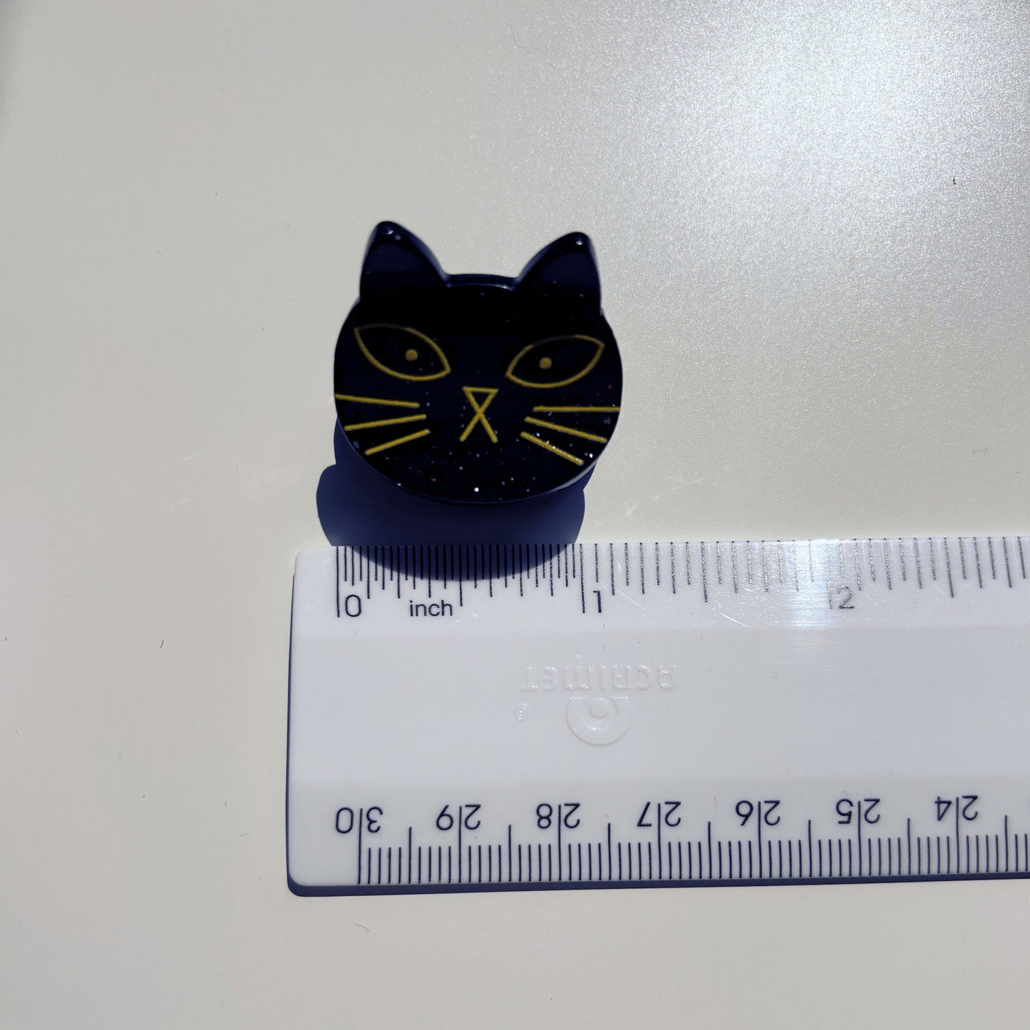 Black cat-shaped object on a white surface with a ruler for scale.