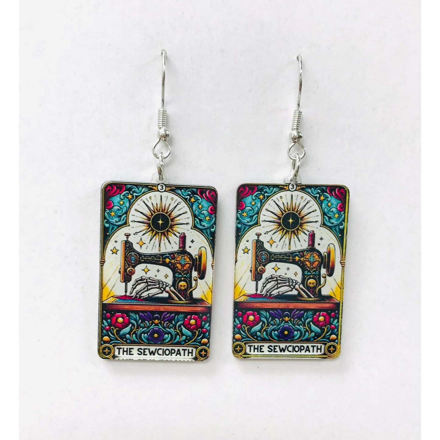 Colorful earrings with a sewing machine design and The Sewciopath text
