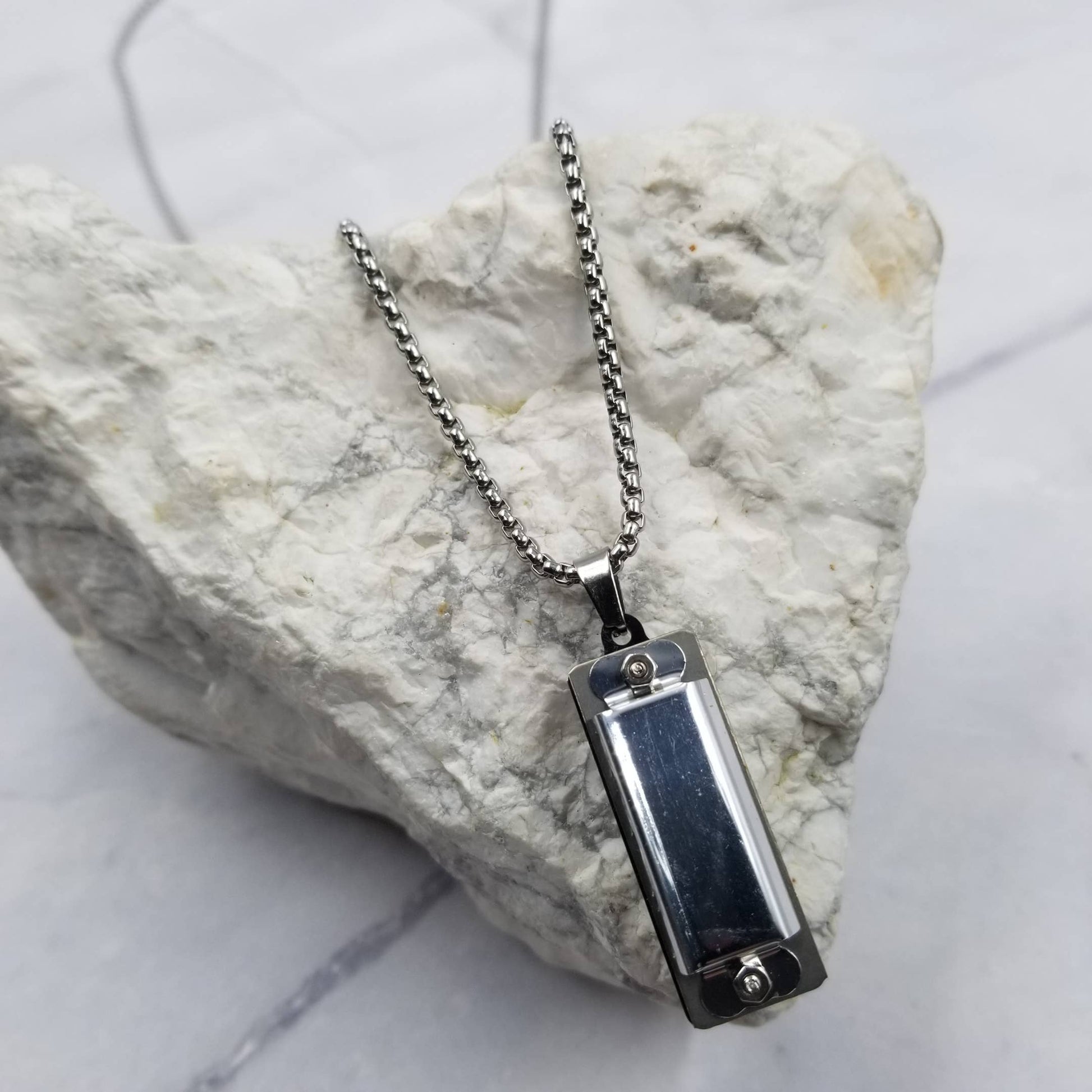 Silver harmonica pendant necklace on a marble surface