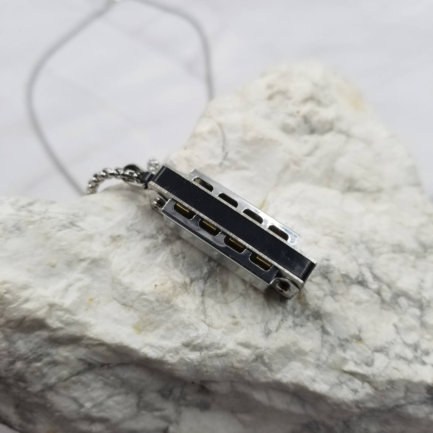 Small black and silver harmonica pendant on a marble surface